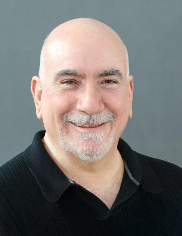 Image of Frank Minano, director of Inland Valley Repertory Theatre. He is wearing a black polo and standing in front of a grey background. 