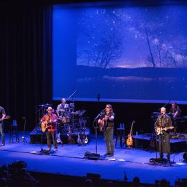 photograph of a band performing on the Lewis Family playhouse stage, with dramatic blue lighting