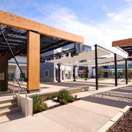 outdoor courtyard stage with a wood and metal canopy over the stage, cloth sun shades over the open are and the Playhouse in the distance.